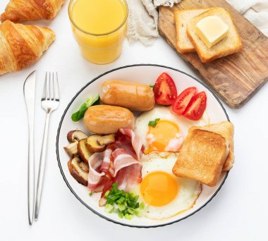 İngiliz kahvaltısı, kızarmış yumurta, sosis, pastırma ve beyaz arka planda tost.