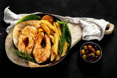 Pişmiş somon bifteği ve kızarmış patatesler siyah arka planda servis ediliyor. Sağlıklı beslenme. Üst görünüm.