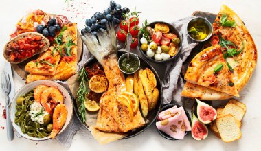 Tabak ve yemek üzerinde İtalyan yemekleriyle dolu bir masa pizza, makarna, salam, parmesan, zeytin, beyaz arka planda ekmek çubukları. Üst görünüm.