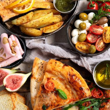 Tabak ve yemek üzerinde İtalyan yemekleriyle dolu bir masa pizza, makarna, salam, parmesan, zeytin, beyaz arka planda ekmek çubukları. Üst görünüm.