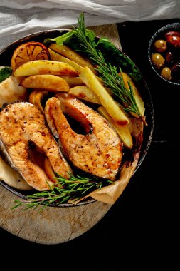 Pişmiş somon bifteği ve kızarmış patatesler siyah arka planda servis ediliyor. Sağlıklı beslenme. Üst görünüm.