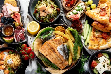 Çeşitli Akdeniz yemekleri - balık, deniz ürünleri, soslar, makarna, atıştırmalıklar, siyah arka planda pizza. Üst görünüm. 