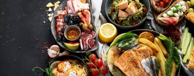 Çeşitli Akdeniz yemekleri - balık, deniz ürünleri, soslar, makarna, atıştırmalıklar, siyah arka planda pizza. Üst Manzara. Kopyalama alanı olan Panorama.