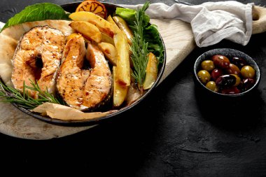 Pişmiş somon bifteği ve kızarmış patatesler siyah arka planda servis ediliyor. Sağlıklı beslenme. Üst Manzara. Boşluğu kopyala.