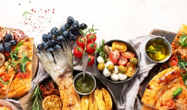 Tabak ve yemek üzerinde İtalyan yemekleriyle dolu bir masa pizza, makarna, salam, parmesan, zeytin, beyaz arka planda ekmek çubukları. Üst Manzara. Boşluğu kopyala.