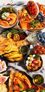 Tabak ve yemek üzerinde İtalyan yemekleriyle dolu bir masa pizza, makarna, salam, parmesan, zeytin, beyaz arka planda ekmek çubukları. Üst görünüm.