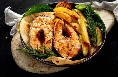 Pişmiş somon bifteği ve kızarmış patatesler siyah arka planda servis ediliyor. Sağlıklı beslenme. Üst görünüm.