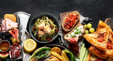 Çeşitli Akdeniz yemekleri - balık, deniz ürünleri, soslar, makarna, atıştırmalıklar, siyah arka planda pizza. Üst Manzara. Boşluğu kopyala.