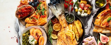 Tabak ve yemek üzerinde İtalyan yemekleriyle dolu bir masa pizza, makarna, salam, parmesan, zeytin, beyaz arka planda ekmek çubukları. Üst Manzara. Kopyalama alanı olan Panorama.