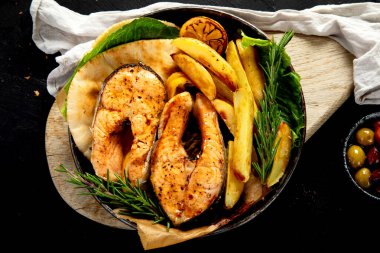 Pişmiş somon bifteği ve kızarmış patatesler siyah arka planda servis ediliyor. Sağlıklı beslenme. Üst görünüm.