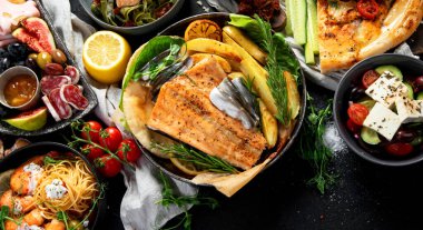 Çeşitli Akdeniz yemekleri - balık, deniz ürünleri, soslar, makarna, atıştırmalıklar, siyah arka planda pizza. Üst görünüm. 