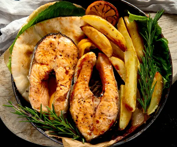 Pişmiş somon bifteği ve kızarmış patatesler siyah arka planda servis ediliyor. Sağlıklı beslenme. Üst Manzara. Boşluğu kopyala.