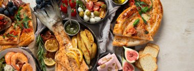 Tabak ve yemek üzerinde İtalyan yemekleriyle dolu bir masa pizza, makarna, salam, parmesan, zeytin, beyaz arka planda ekmek çubukları. Üst Manzara. Kopyalama alanı olan Panorama.