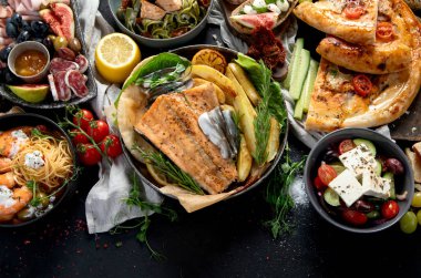 Çeşitli Akdeniz yemekleri - balık, deniz ürünleri, soslar, makarna, atıştırmalıklar, siyah arka planda pizza. Üst Manzara. Boşluğu kopyala.
