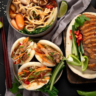 Koyu arkaplanda Çin yemekleri: tatlı ve ekşi ördek, erişte çorbası, buğulanmış çörekler. Asya tarzı ziyafet ya da açık büfe, üst görünüm