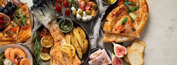 Tabak ve yemek üzerinde İtalyan yemekleriyle dolu bir masa pizza, makarna, salam, parmesan, zeytin, beyaz arka planda ekmek çubukları. Üst Manzara. Kopyalama alanı olan Panorama.