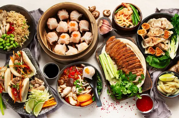 Koyu arkaplanda Çin yemekleri: tatlı ördek, çorba, buharda pişmiş çörekler, bambu buharlı buhar tenceresi, salata, pilav, sos. Asya tarzı ziyafet, üst görünüm. 