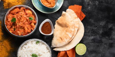Hint tereyağlı tavuk, basmati pilavı, baharatlar, siyah arka planda bir tabakta naan ekmeği. Tavuk tikka masala. Geleneksel Hint yemeği konsepti. Üst Manzara. Kopyalama alanı olan Panorama.
