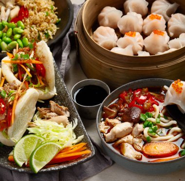 Koyu arkaplanda Çin yemekleri: tatlı ördek, çorba, buharda pişmiş çörekler, bambu buharlı buhar tenceresi, salata, pilav, sos. Asya usulü ziyafet, en iyi manzara. Boşluğu kopyala.