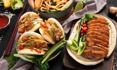 Koyu arkaplanda Çin yemekleri: tatlı ve ekşi ördek, erişte çorbası, buğulanmış çörekler. Asya tarzı ziyafet ya da açık büfe, üst görünüm