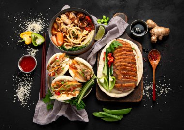 Koyu arkaplanda Çin yemekleri: tatlı ve ekşi ördek, erişte çorbası, buğulanmış çörekler. Asya tarzı ziyafet ya da açık büfe, üst görünüm