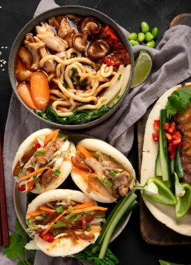 Koyu arkaplanda Çin yemekleri: tatlı ve ekşi ördek, erişte çorbası, buğulanmış çörekler. Asya tarzı ziyafet ya da açık büfe, üst görünüm