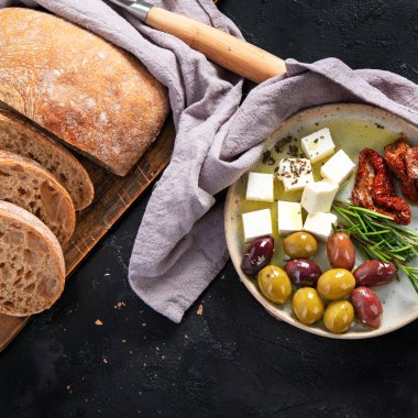 Koyu arkaplanda zeytin, zeytinyağı ve ciabatta ekmeği. Üst görünüm.