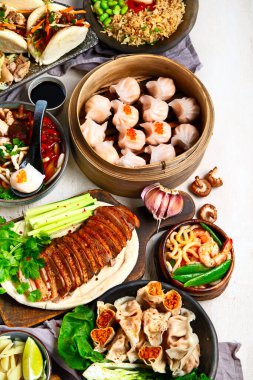 Koyu arkaplanda Çin yemekleri: tatlı ördek, çorba, buharda pişmiş çörekler, bambu buharlı buhar tenceresi, salata, pilav, sos. Asya usulü ziyafet, en iyi manzara. Boşluğu kopyala.