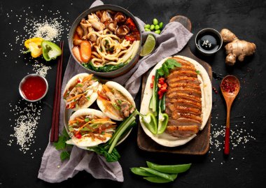 Koyu arkaplanda Çin yemekleri: tatlı ve ekşi ördek, erişte çorbası, buğulanmış çörekler. Asya tarzı ziyafet ya da açık büfe, üst görünüm