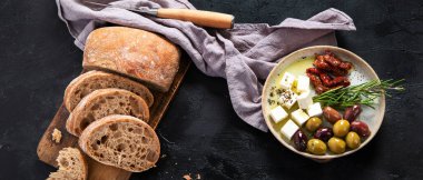 Koyu arkaplanda zeytin, zeytinyağı ve ciabatta ekmeği. Üst Manzara. Panorama.