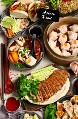 Koyu arkaplanda Çin yemekleri: tatlı ördek, çorba, buharda pişmiş çörekler, bambu buharlı buhar tenceresi, salata, pilav, sos. Asya usulü ziyafet, en iyi manzara. Boşluğu kopyala.