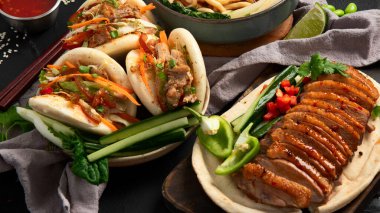 Koyu arkaplanda Çin yemekleri: tatlı ve ekşi ördek, erişte çorbası, buğulanmış çörekler. Asya tarzı ziyafet ya da açık büfe, üst görünüm