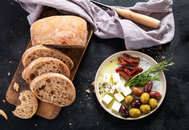 Koyu arkaplanda zeytin, zeytinyağı ve ciabatta ekmeği. Üst görünüm.