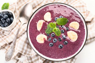 Beyaz arka planda sağlıklı kahvaltı için taze yaban mersinli meyve suyu kasesi. Üst görünüm. 