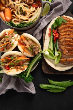 Koyu arkaplanda Çin yemekleri: tatlı ve ekşi ördek, erişte çorbası, buğulanmış çörekler. Asya tarzı ziyafet ya da açık büfe, üst manzara. Boşluğu kopyala