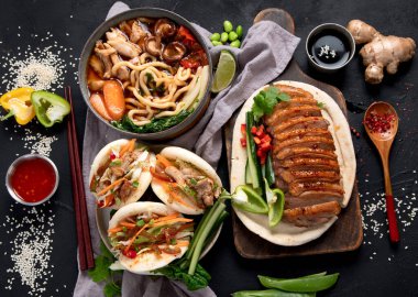 Koyu arkaplanda Çin yemekleri: tatlı ve ekşi ördek, erişte çorbası, buğulanmış çörekler. Asya tarzı ziyafet ya da açık büfe, üst görünüm