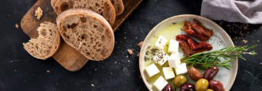 Koyu arkaplanda zeytin, zeytinyağı ve ciabatta ekmeği. Üst Manzara. Kopyalama alanı olan Panorama.