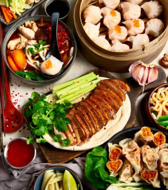 Koyu arkaplanda Çin yemekleri: tatlı ördek, çorba, buharda pişmiş çörekler, bambu buharlı buhar tenceresi, salata, pilav, sos. Asya tarzı ziyafet, üst görünüm. 