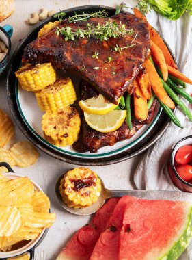 Sebzeli barbekü kaburgası, sos, kavrulmuş mısır ve beyaz arka planda karpuz. Üst görünüm.