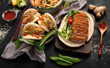 Koyu arkaplanda Çin yemekleri: tatlı ve ekşi ördek, erişte çorbası, buğulanmış çörekler. Asya tarzı ziyafet ya da açık büfe, üst görünüm