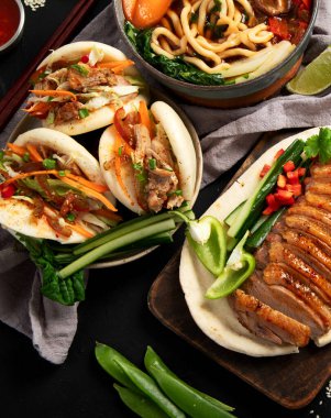 Koyu arkaplanda Çin yemekleri: tatlı ve ekşi ördek, erişte çorbası, buğulanmış çörekler. Asya tarzı ziyafet ya da açık büfe, üst görünüm