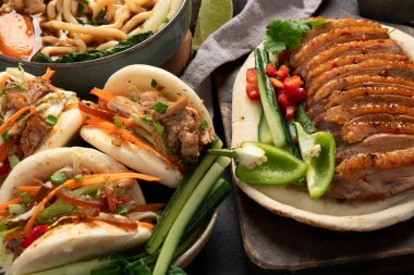 Koyu arkaplanda Çin yemekleri: tatlı ve ekşi ördek, erişte çorbası, buğulanmış çörekler. Asya tarzı ziyafet ya da açık büfe, üst görünüm