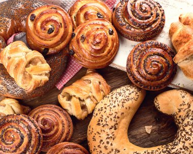 Ekmek, çörek, kruvasan. Ahşap arka planda çeşitli fırın malzemeleri var. Kahvaltı konsepti. Üst görünüm.