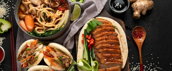 Koyu arkaplanda Çin yemekleri: tatlı ve ekşi ördek, erişte çorbası, buğulanmış çörekler. Asya tarzı ziyafet ya da açık büfe, üst manzara. Kopyalama alanı olan Panorama