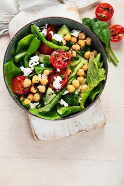 Domates, salatalık, salata, nohut ve peynirli vejetaryen nohut salatası hafif bir arka planda. Sağlıklı bir yaşam tarzı. Üst görünüm, alanı kopyala.