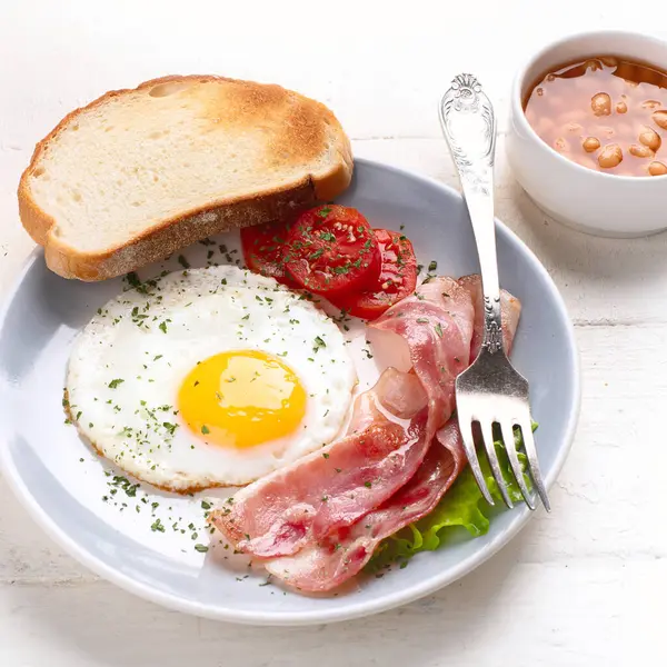 Yağda yumurta, pastırma, domates ve beyaz arka planda tost. Üst görünüm.