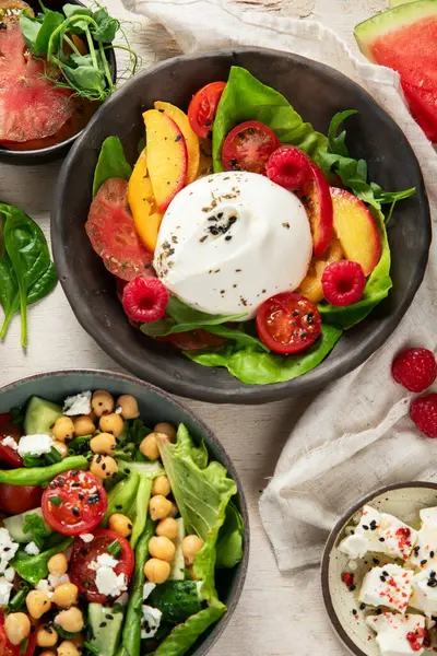 Çilekli çeşitli yaz salataları, otlar. Hafif arkaplanlı sağlıklı salata, şeftali, burrata, yabanmersini ve ceviz. Sağlıklı yemek için taze yararlı yemek. Üst görünüm.