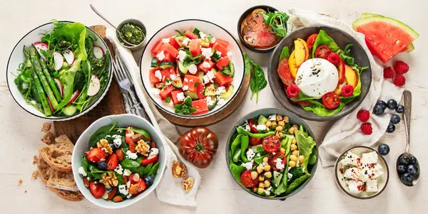 Çilekli çeşitli yaz salataları, otlar. Hafif arkaplanlı sağlıklı salata, şeftali, burrata, yabanmersini ve ceviz. Sağlıklı yemek için taze yararlı yemek. Üst görünüm.