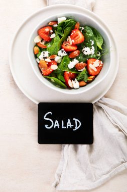 Ispanak ve çilekli yaz salatası süzme peynir ve hafif arka planda badem. Üst Manzara. Boşluğu kopyala.