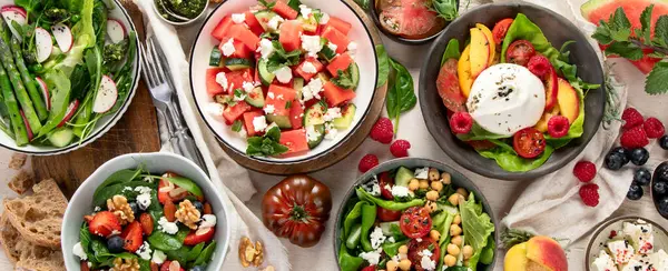 Çilekli çeşitli yaz salataları, otlar. Hafif arkaplanlı sağlıklı salata, şeftali, burrata, yabanmersini ve ceviz. Sağlıklı yemek için taze yararlı yemek. Üst Manzara. Panorama.
